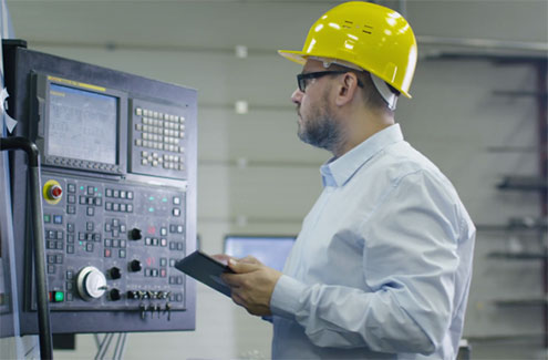 worker with a hard hat and clipboard at a control panel