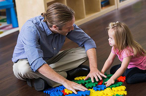 male teacher playing with a young child on the floor
